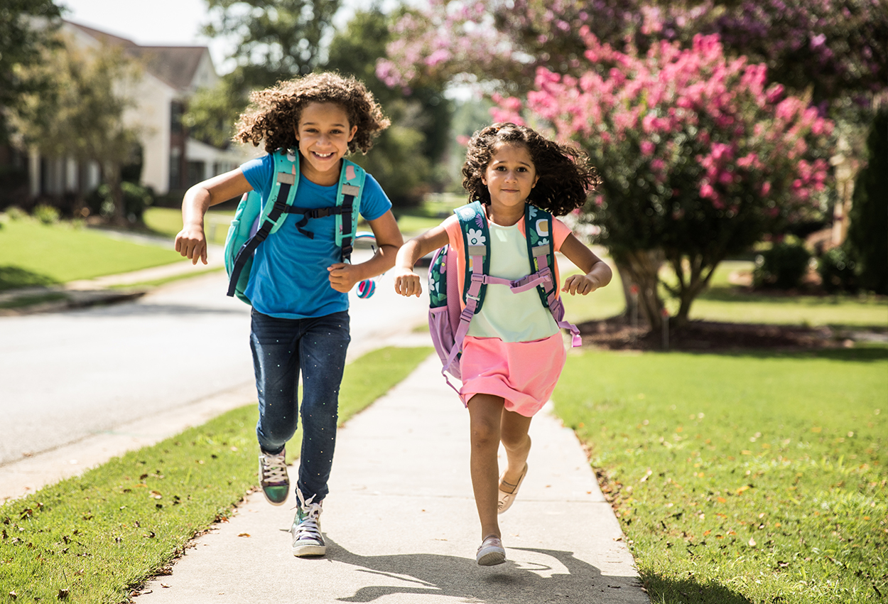 Children running on sidewalk with backpacks