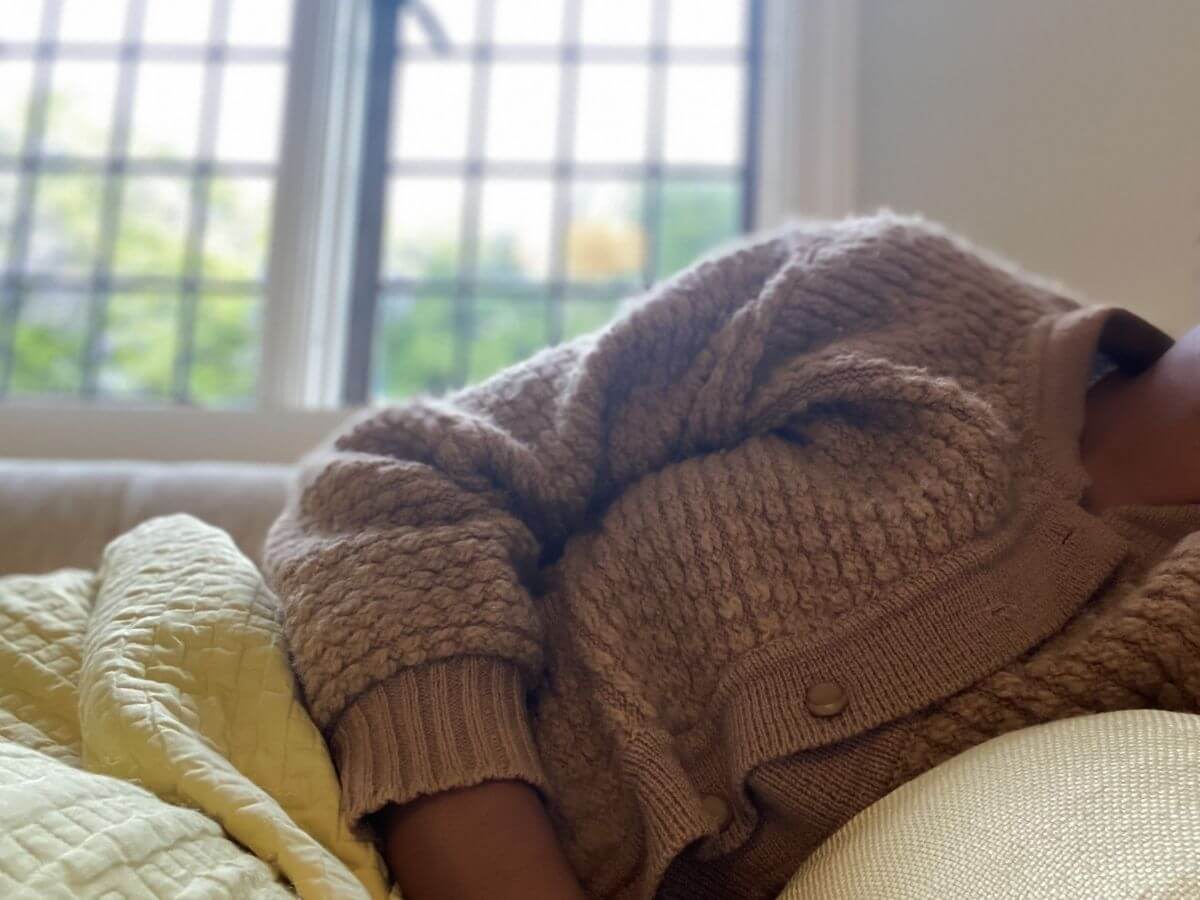 Close up of a woman's torso. The woman is laying in bed under the covers during the day.