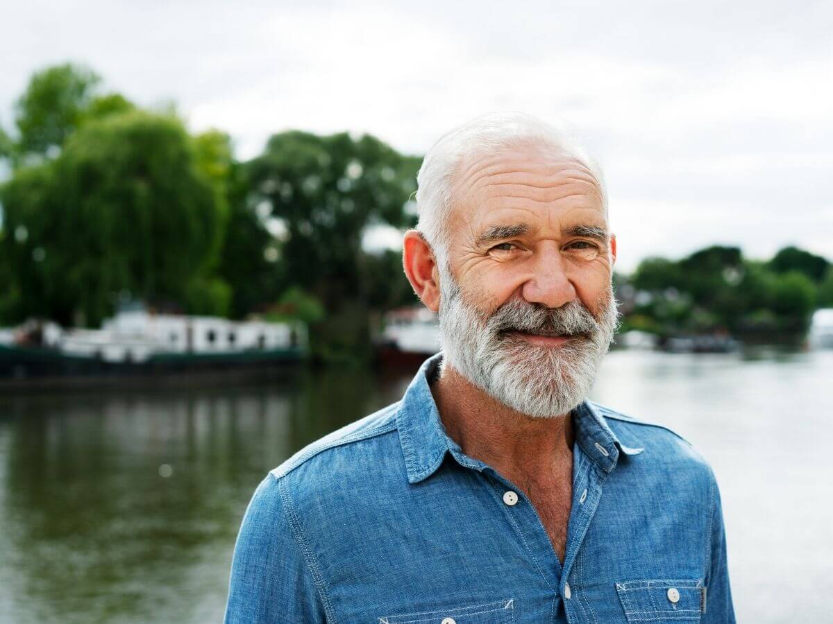 Photo of an older, white-haired man standing in front of a lake