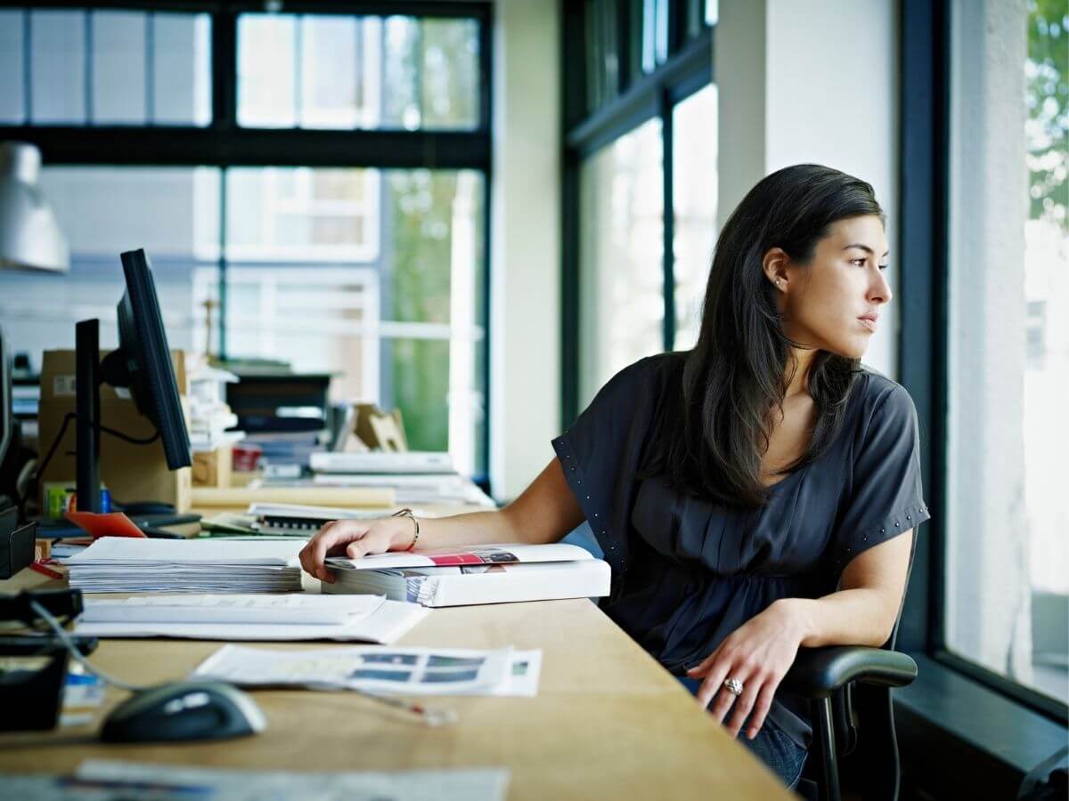 Young woman stares vacantly out the window in her office at work