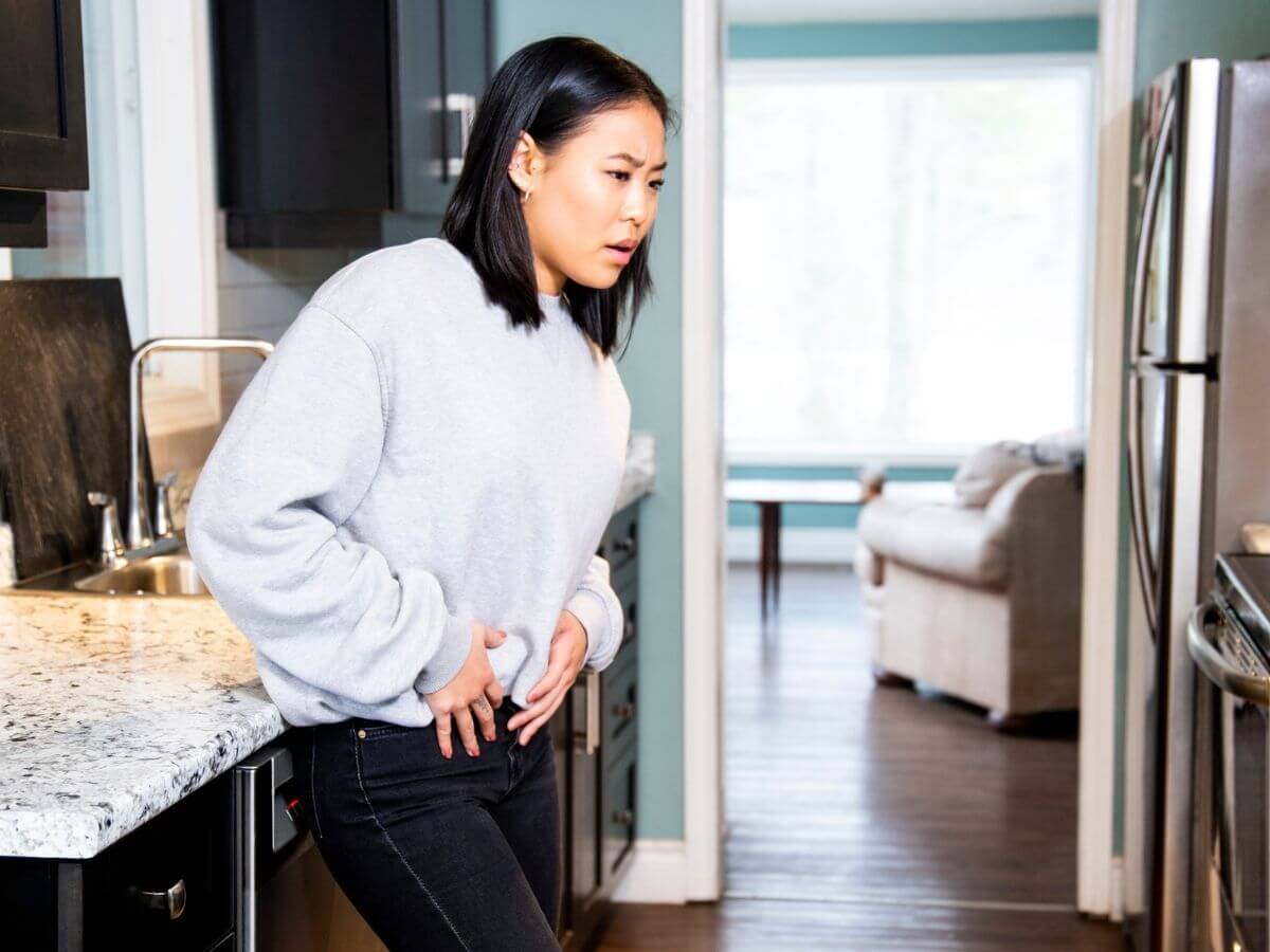 Woman stands in her kitchen and holds her pelvis in pain