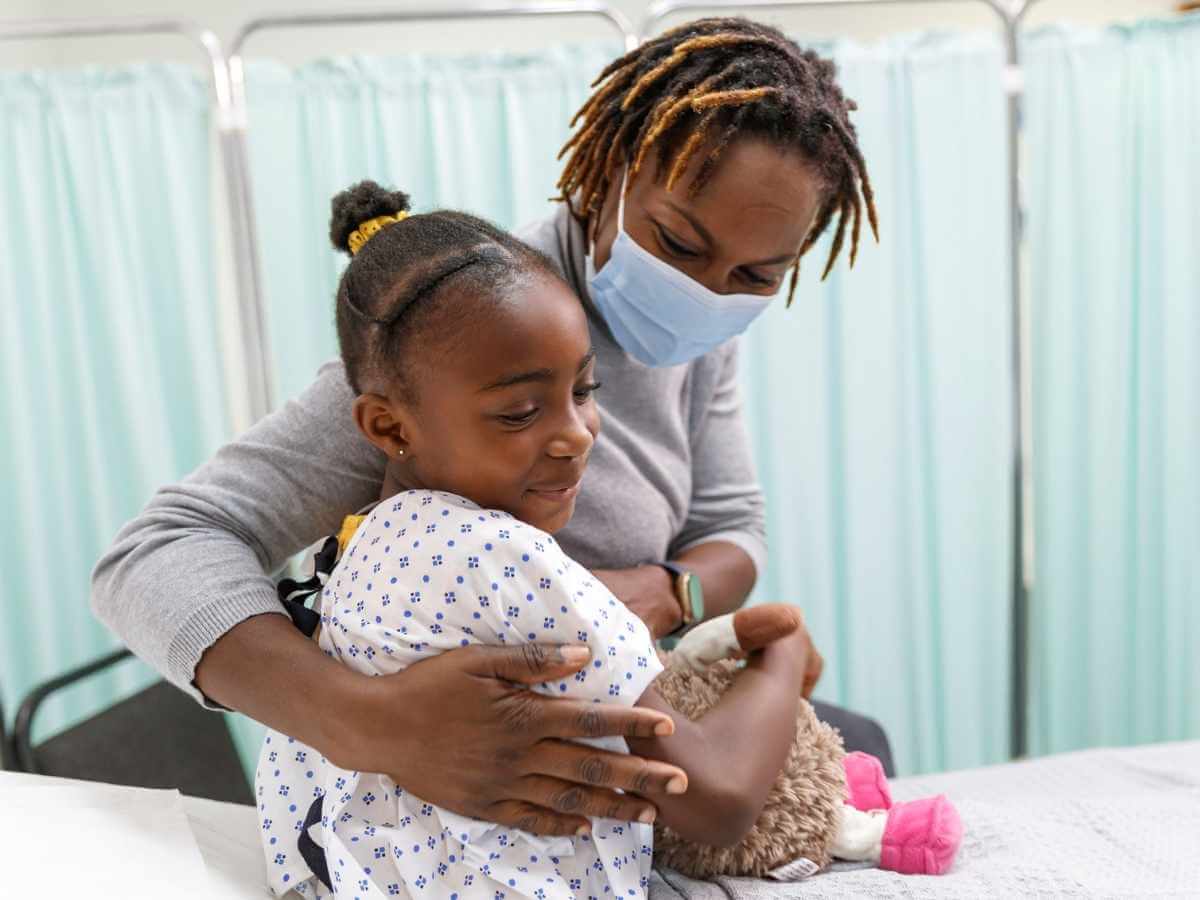 Mother comforts young daughter who is in a hospital gown on a stretcher prior to a procedure