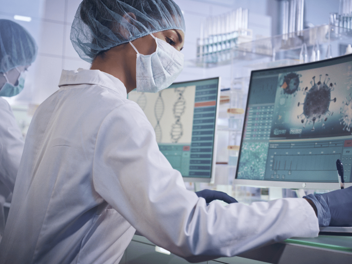 Laboratory team during coronavirus lab tests. Wearing protective masks and caps. Looking at COVID-19 virus data on computer screens.