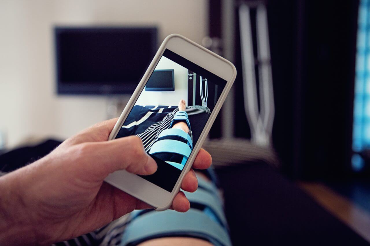 Man lying in hospital bed and take pictures of his injured knee.